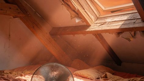 Chambre mansardée avec poutres apparentes, lit sous plafond en pente, lumière vive traversant fenêtre de toit, ombres graphiq